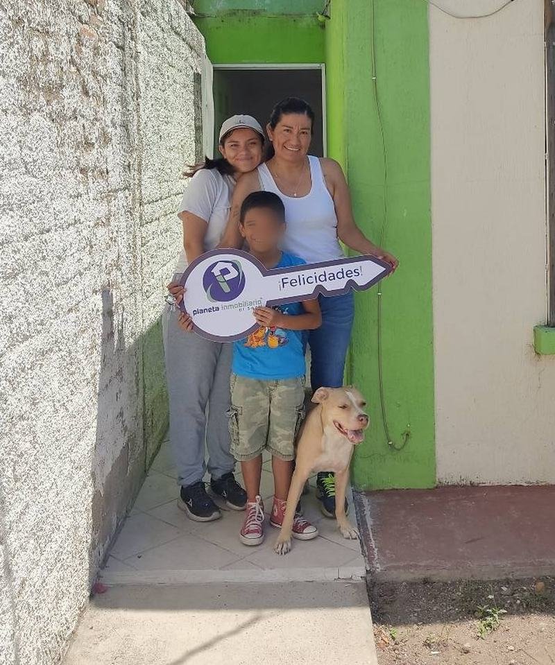 Una familia frente a su casa sosteniendo una llave con el mensaje Felicidades